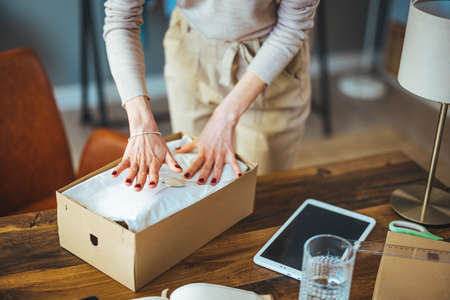 Cropped image of young woman packing things in cardboard box while working in officeの写真素材