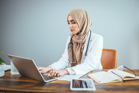Portrait of muslim female doctor working with laptop in office.