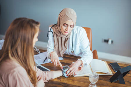 Muslim female doctor and patient discussing something while sitting at the table.の写真素材