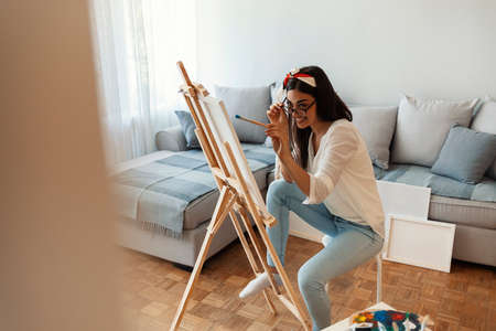 Young woman painting a picture on easel in the living room at homeの写真素材