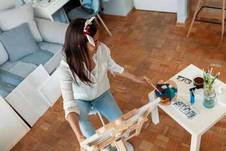 Beautiful young woman artist painting a picture on canvas at home.の写真素材