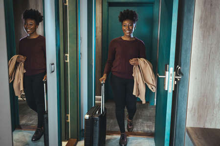 Young african american woman with luggage entering hotel room and smiling.の写真素材