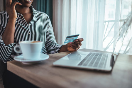 Cropped image of young african american woman holding credit card and using laptop in cafe