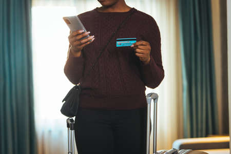 Cropped image of african american woman using smartphone and holding credit card while standing in hotel roomの写真素材