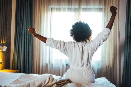 Young african american woman stretching in bed after wake up.の写真素材