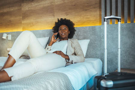 Young african american woman talking on mobile phone in hotel roomの写真素材