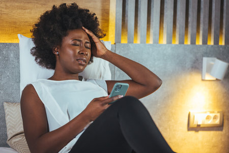 Young african american woman using smartphone while sitting on bed at home