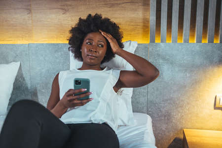 Woman using mobile phone while sitting on bed at homeの写真素材