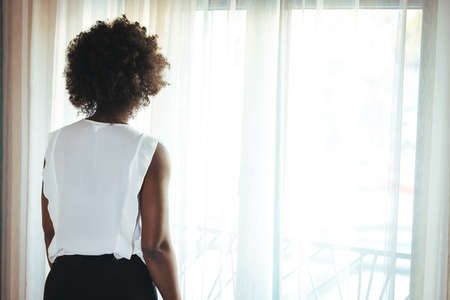 Back view of young african american businesswoman looking out the windowの写真素材