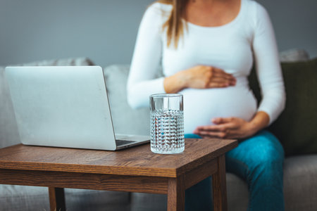Pregnant woman working at home with laptop and glass of water