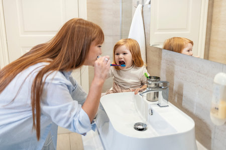 Mother and daughter brushing teeth in bathroom. Mom and little girl cleaning teethの写真素材