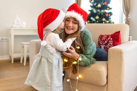 Christmas, holidays and people concept - happy mother and daughter in santa helper hats decorating christmas tree at homeの写真素材