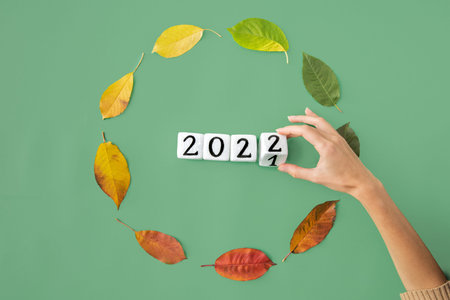Life cycle time movement in circular form manifested by leaves in collors from green, yellow, red and brown flat lay on aqua background representing a year of life of a tree or human with a happy new year 2022 cubes year change by handの写真素材