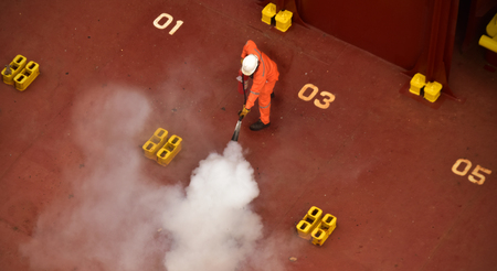 Seaman extinguishing staged fire as part of regular monthly training and testing of equipment on board a cargo ship. Wearing personal protective equipment using fire extinguisher. Great concept for maritime safety related publications.の写真素材