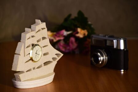 Model of a sailing ship with installed clock, old photocamera and bunch of flowers on a table. Concept for time,  and traditional, vintage.の写真素材