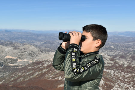 Boy at the top of the mountain observing birds with his binocular.のeditorial素材