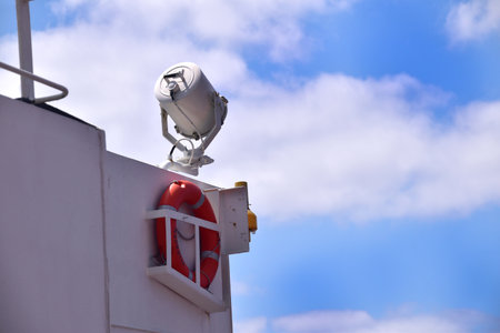 Search light on the side of the navigational bridge against blue sky. Below is life ring or man over board buoy with smoke and light signal.の写真素材