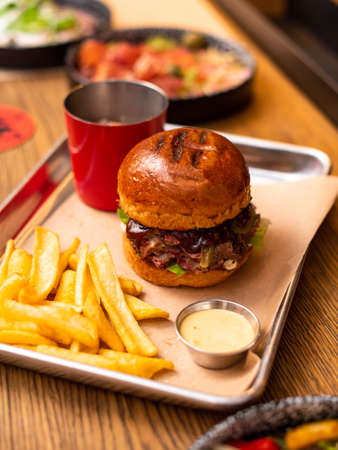 Tasty grilled burger with beef,cheese,bacon and sauce on wooden table with french fries and beerの写真素材