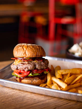 Tasty grilled burger with beef,cheese,bacon and sauce on wooden table with french fries and beerの写真素材