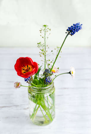 Small bouquet of spring field flowers in a glass jar on white wooden rustic backgroundの写真素材
