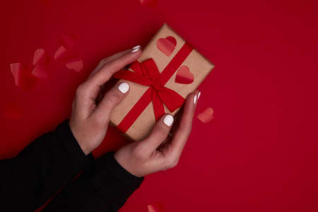 Valentine day composition. Hand holding gift box with ribbon bow and red hearts confetti.の写真素材