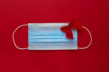 Festive face mask with decorations on red background. Flat lay, top view christmas holiday composition. New year wallpaper bannerの写真素材