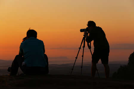 Silhouette photographer and friend of her shooting on sunrise and watching sunrise on the hill.の写真素材