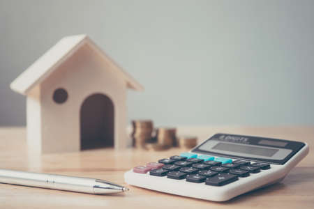 Calculator with wooden house and coins stack and pen on wood table. Property investment and house mortgage financial conceptの写真素材