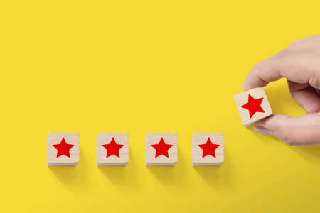 Hand putting wood block with five star symbol to increase rating of company with yellow background, Copy space for text or headlineの写真素材