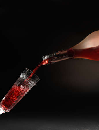 Red wine pouring into wine glass on black backgroundの写真素材