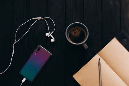 Bright colorful smartphone on a black wooden background. Morning cup of coffee.の写真素材