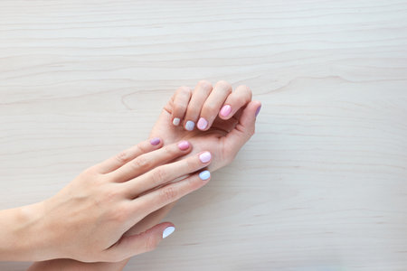 Stylish trendy female pastel white, pink and blue manicure. Beautiful young womans hands on wooden background. Copy space bannerの写真素材