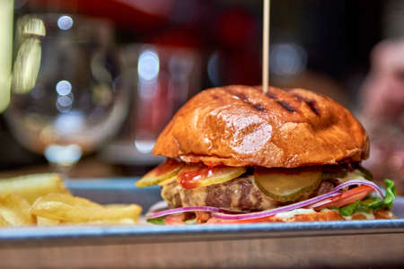 Tasty grilled burger with beef,cheese,bacon and sauce on wooden table with french fries and beerの写真素材