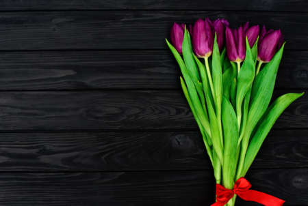 Bouquet of purple spring tulip flowers on a black wooden background. Flat lay. Copy space. Mothers Day. International Womens Day.の写真素材