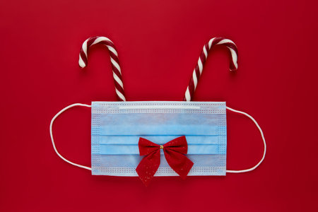 Festive reindeer made from face mask and decorations on red background. Flat lay, top view christmas holiday composition. New year wallpaper bannerの写真素材