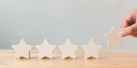 Hand putting wooden five star shape on table. The best excellent business services rating customer experience conceptの写真素材