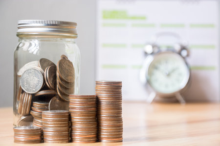 Concept business finance save money, Coins stack on wood table with blurred calendar and alarm clockの写真素材