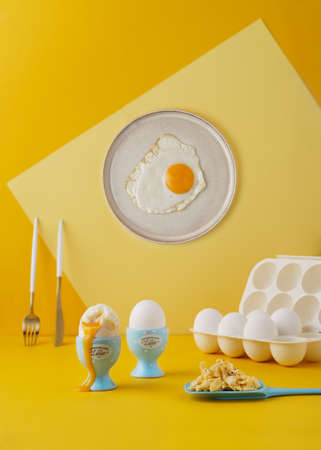 Eggs cooked three different ways on vibrant yellow background, with surreal elements as plate on the wall.の写真素材