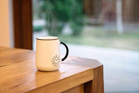 A soaring white cup with a picture of a pocket watch on a wooden table.の写真素材