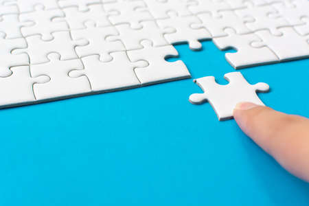 Hand putting piece of white jigsaw puzzle on blue background. Team business success partnership or teamwork.の写真素材