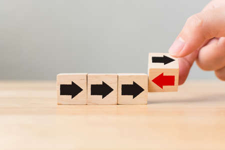 Hand flip over wooden cube block with red arrow facing the opposite direction black arrows, Unique, think different, individual and standing out from the crowd conceptの写真素材