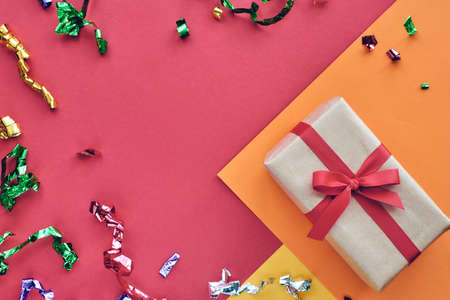 Christmas composition. Giftbox with red ribbon and confetti decorations on pastel paper colorful background. Christmas, winter, new year celebration concept. Flat lay, top view, copy spaceの写真素材