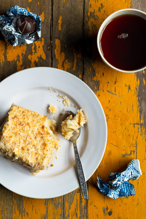 Homemade mille-feuille, puff pastry custard cream pie on white plate, chocolates, tea cup on old yellow woodの写真素材