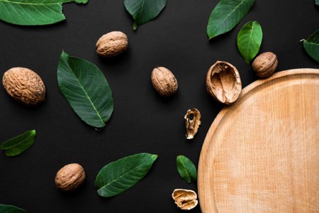 Closeup nutshell and fresh green leafs on a black background. Part of wooden cutting board