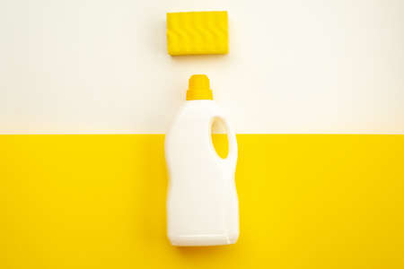 Detergent bottle with yellow cap and sponge on a white-yellow backgroundの写真素材