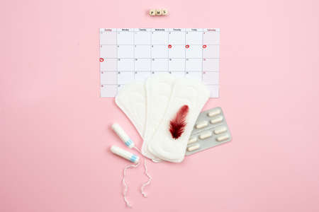 Tampon, feminine, sanitary pads for critical days, feminine calendar, pain pills during menstruation and a red feather on a pink background. Care of hygiene during menstruation.の写真素材