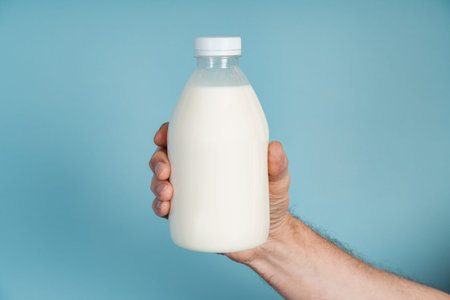 Male hand holds a bottle of milk on a blue background.