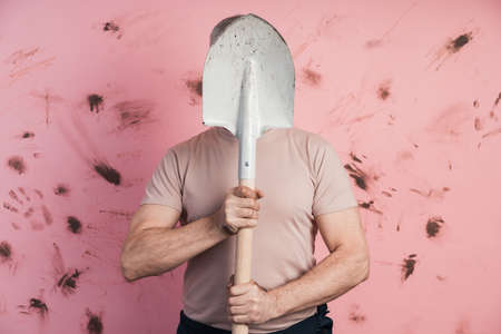 Man hid behind a shovel on a pink background. The concept of housekeeping, farming, gardeningの写真素材