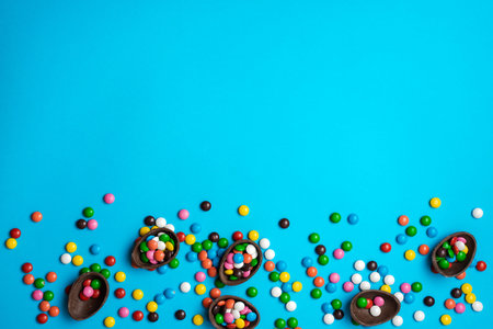 Easter chocolate egg with colorful explosion of candies and sweets on a blue background. Flat lay....
