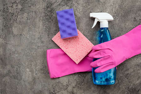 Household accessories: washing spray, spongy and latex gloves lying on a gray decorative plaster background.の写真素材